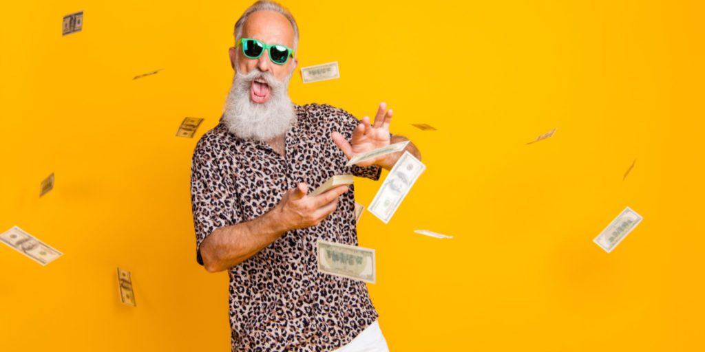 bearded man in leopard shirt stands in front of an orange background, flicking money into the air
